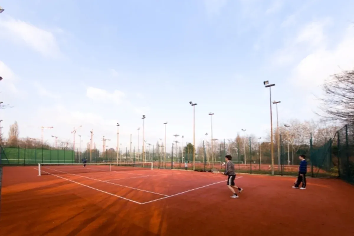 Courts extérieurs du parc municipal Suzanne Lenglen avec joueurs, clôtures et éclairage