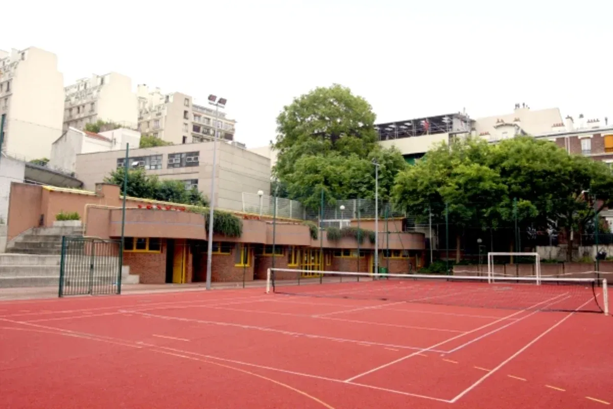 Court extérieur rouge du tennis Jandelle, entouré d’arbres et de bâtiments